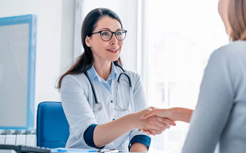 A physician shaking hands with a patient in a bright consultation room